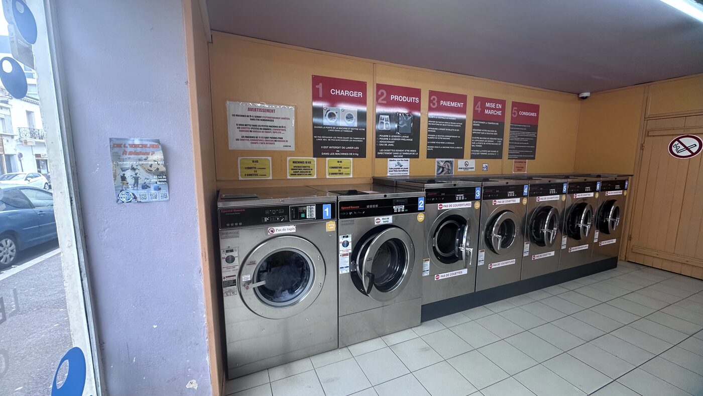 Intérieur de la Laverie du Coin, laverie automatique en libre-service à Béziers, avec ses machines à laver professionnelles en inox et le mode d'emploi affiché